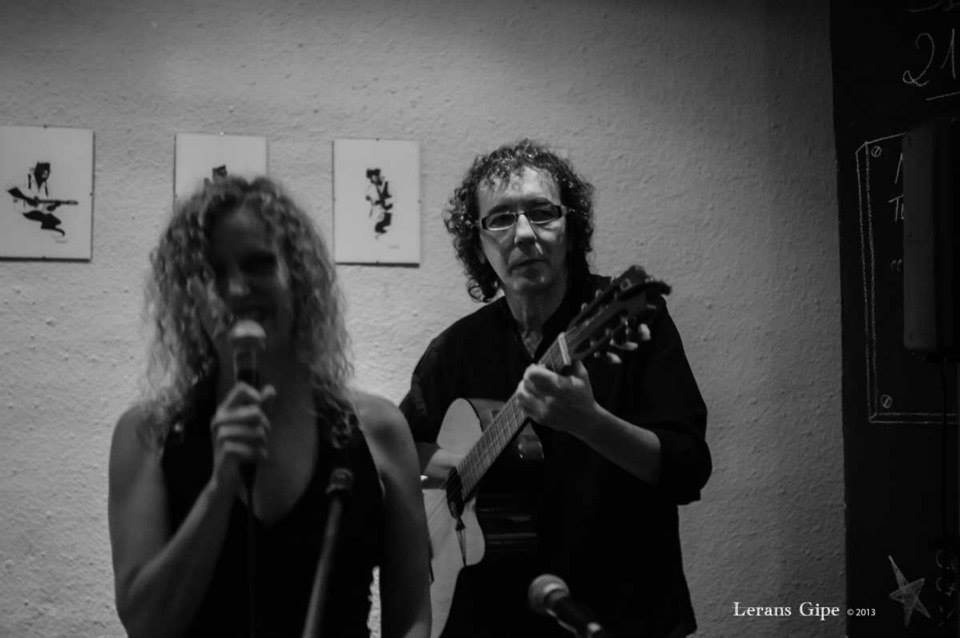 Mike y Mona en una sala blanca: él a la guitarra y ella cantando con vestido largo negro y guantes