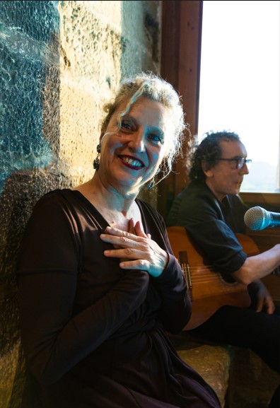 Mona sonríe con la mano en el pecho junto a Mike a la guitarra, en un interior de piedra en el Matarraña