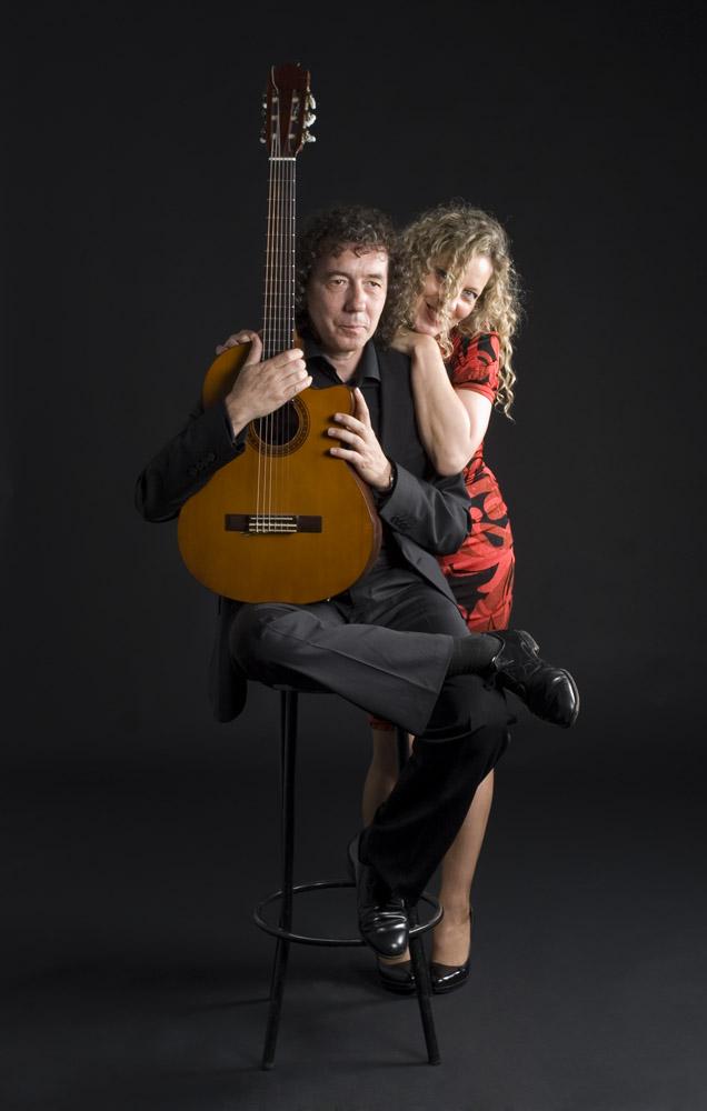 Retrato de estudio: Mike sentado en un taburete abrazando la guitarra y Mona apoyada en su hombro con vestido rojo