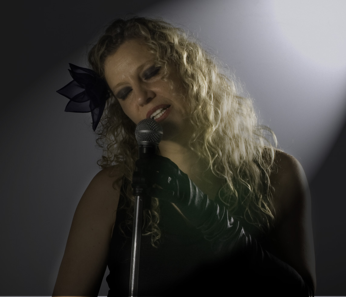 Retrato de Mona cantando con una flor oscura en el pelo, iluminada por un foco lateral
