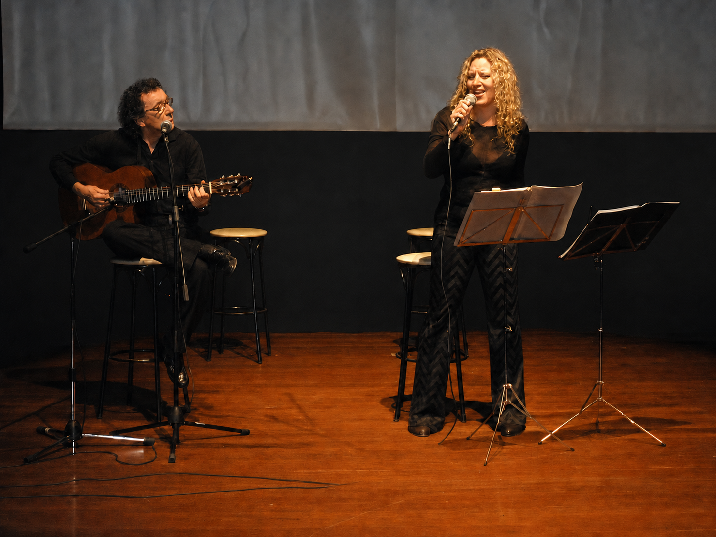 Mike y Mona en escena en un teatro, con taburetes y atriles sobre un suelo de madera